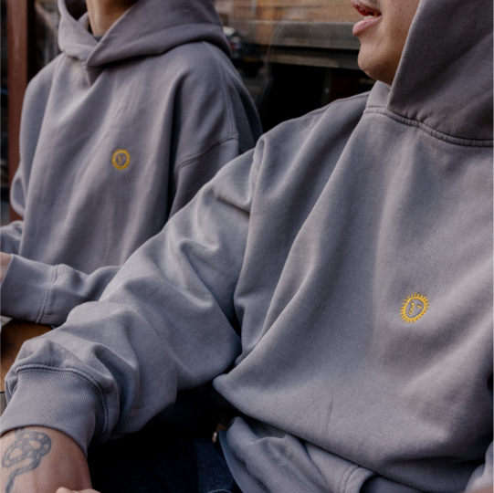 Two people wearing gray hoodies with a logo, sitting close together.