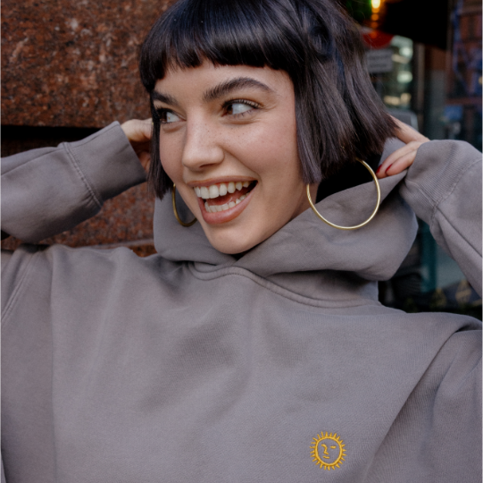 Woman wearing a gray hoodie with a Federal logo, smiling outdoors.